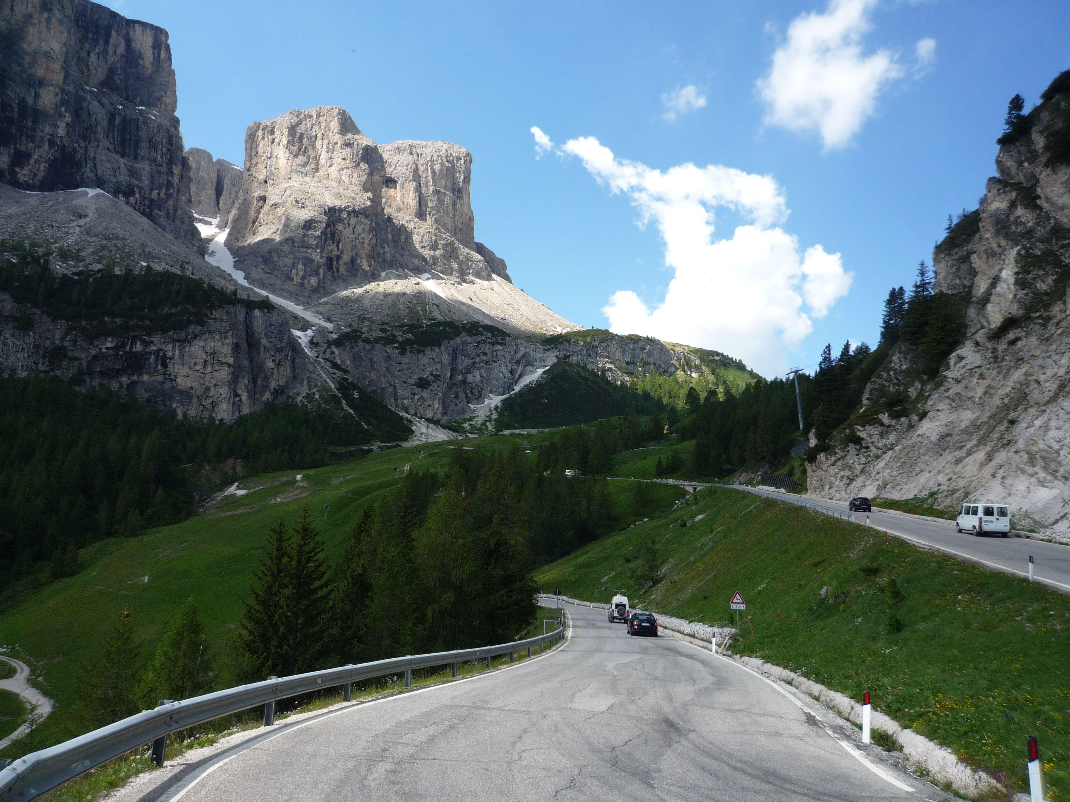 The road on Passo Gardena winding between green slopes and sheer limestone walls