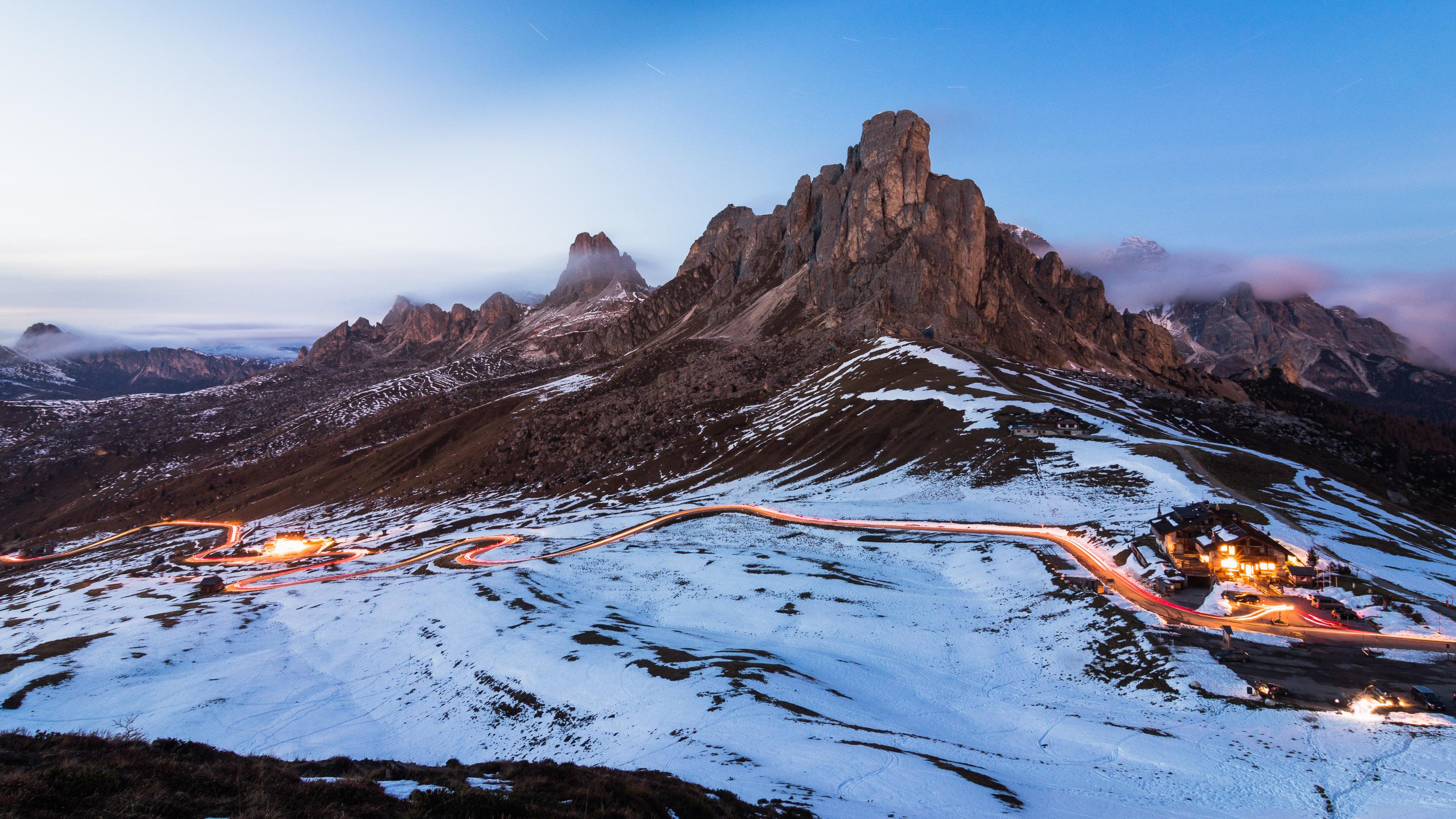 A mountain road below rocky slopes and drifting cloud at Passo Giau