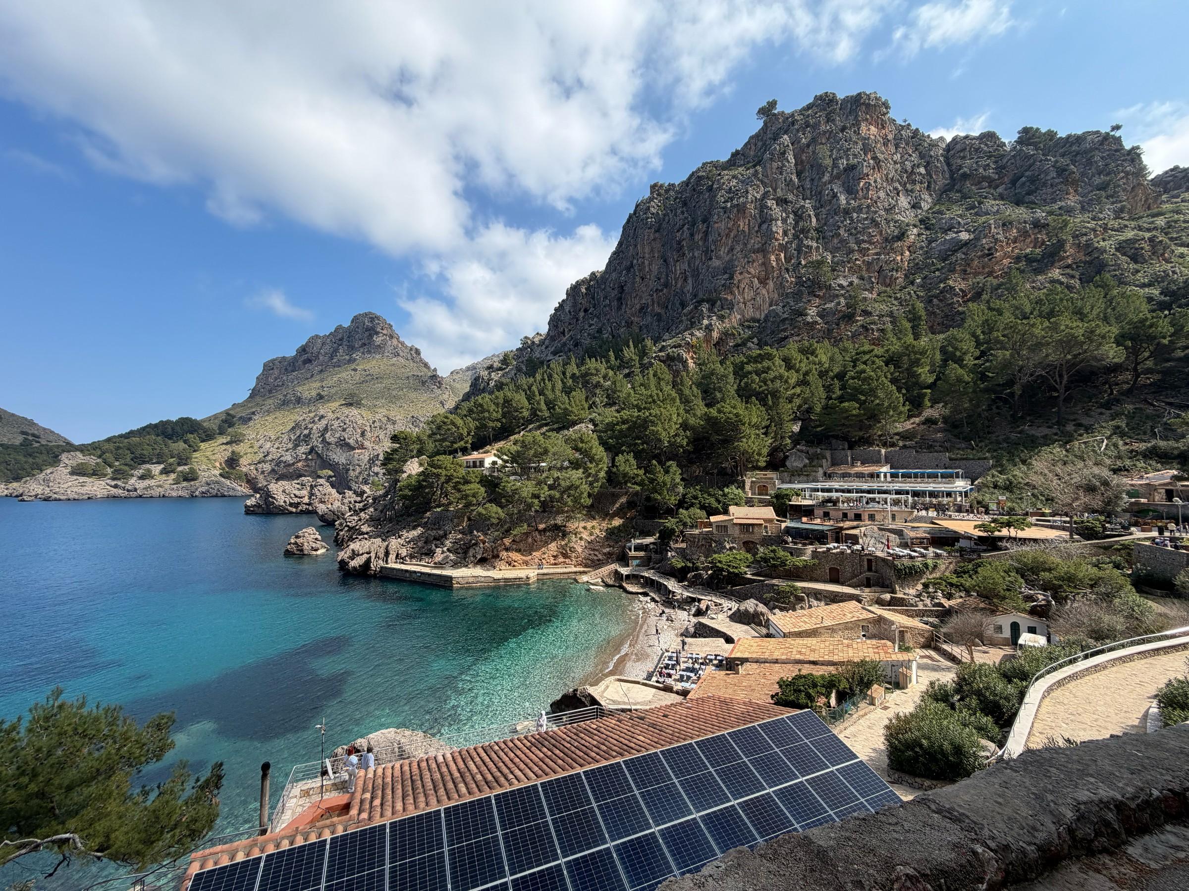 Waterfront buildings and a small beach at Sa Calobra beneath wooded cliffs