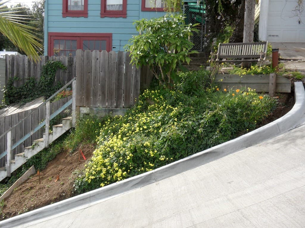 Side view of Bradford Street’s concrete ramp beside garden steps, a fence and houses in San Francisco