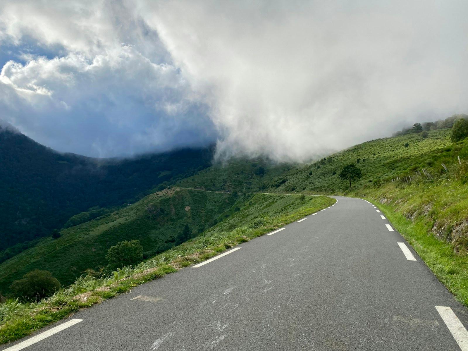 The road at Col d’Aspin curving around green slopes beneath low cloud