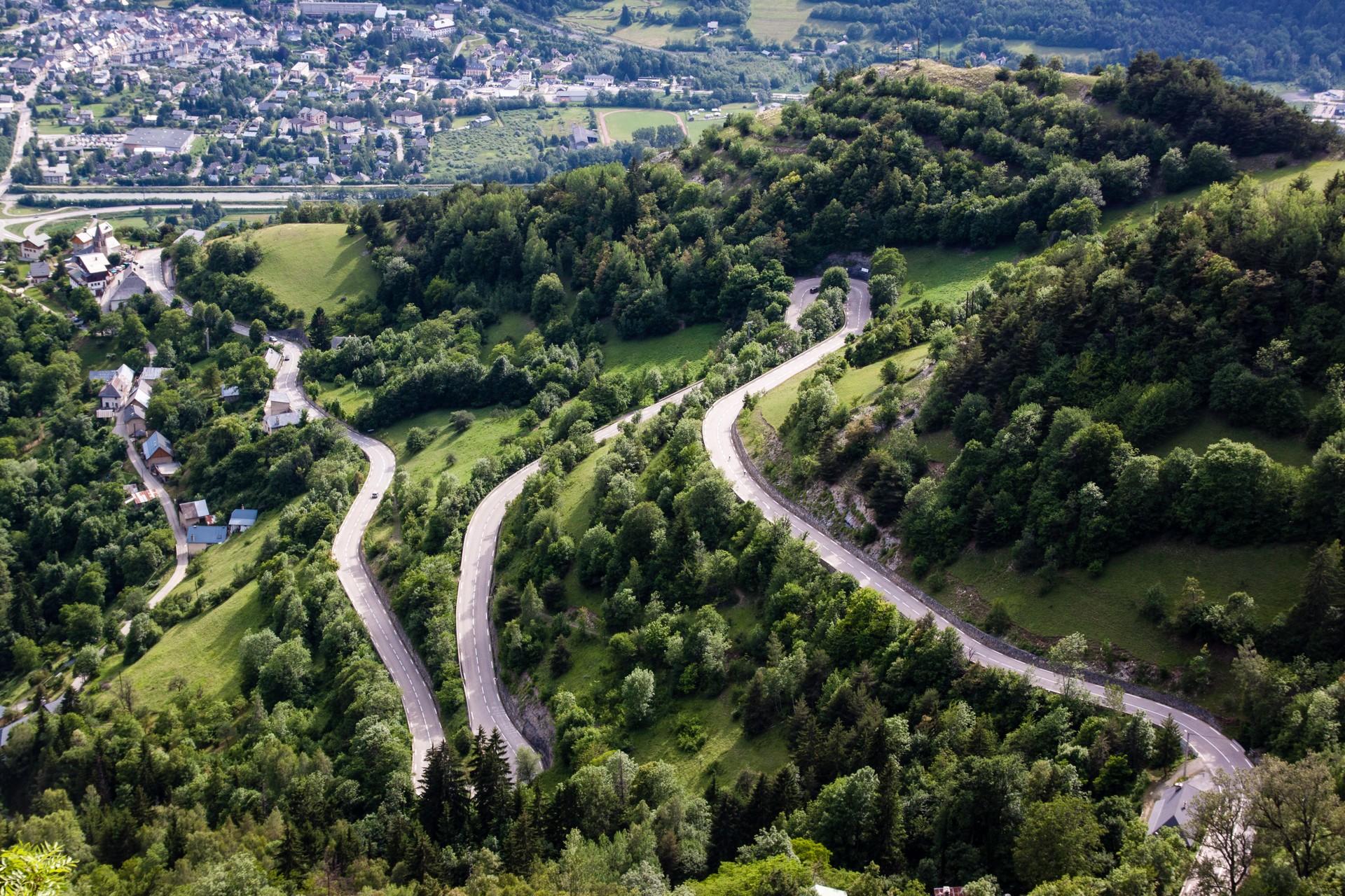 Hairpin bends winding through trees on Alpe d’Huez, with Bourg d’Oisans in the valley below